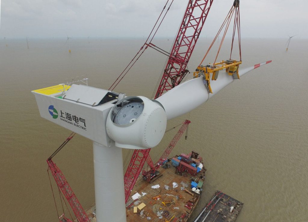 Aerial view of a wind turbine being installed over the sea, showcasing renewable energy construction.